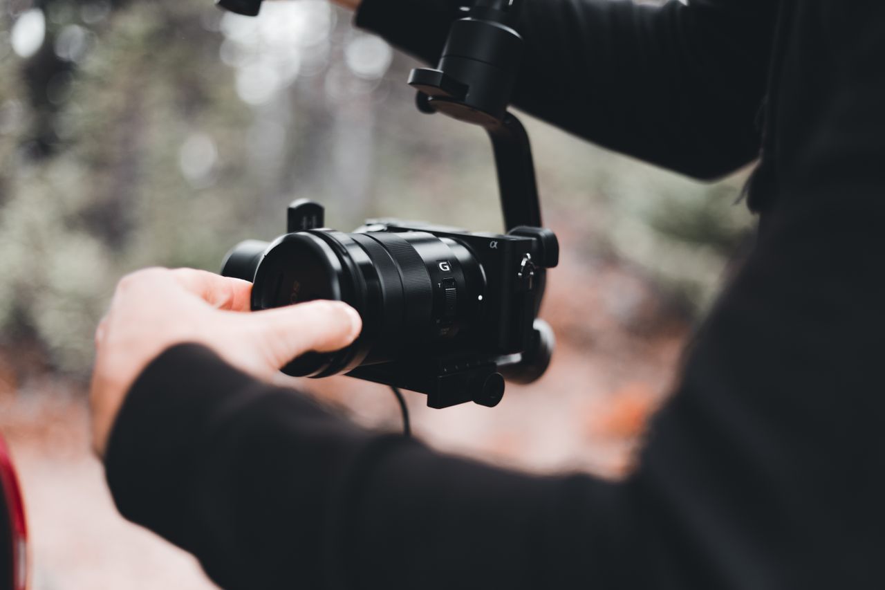Man adjusting camera on stabilizer in a forest setting, captured in shallow focus.
